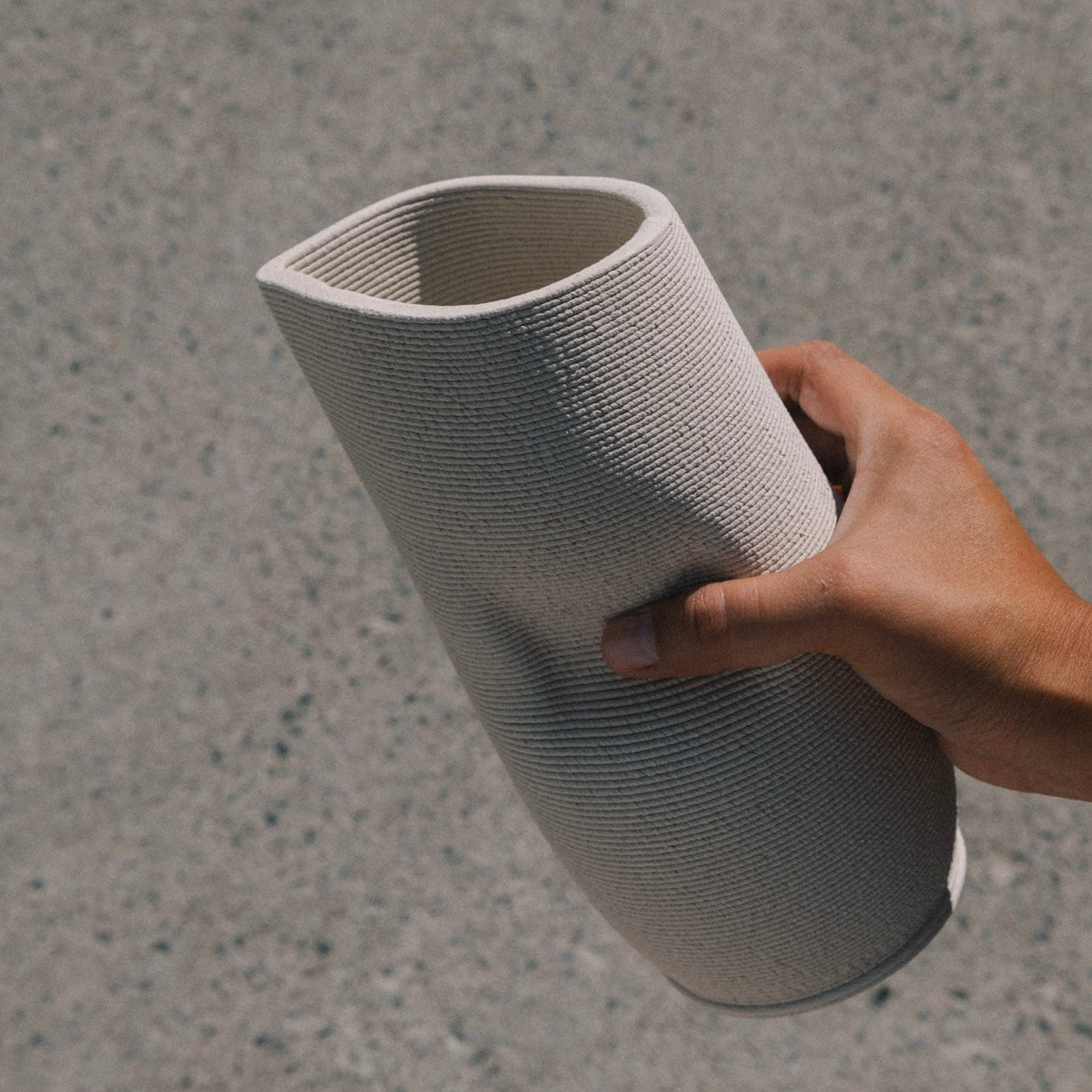 Hand holding 3D printed ceramic pitcher in natural stoneware clay, minimal design, handmade in Berlin, showcasing textured surface and modern form.