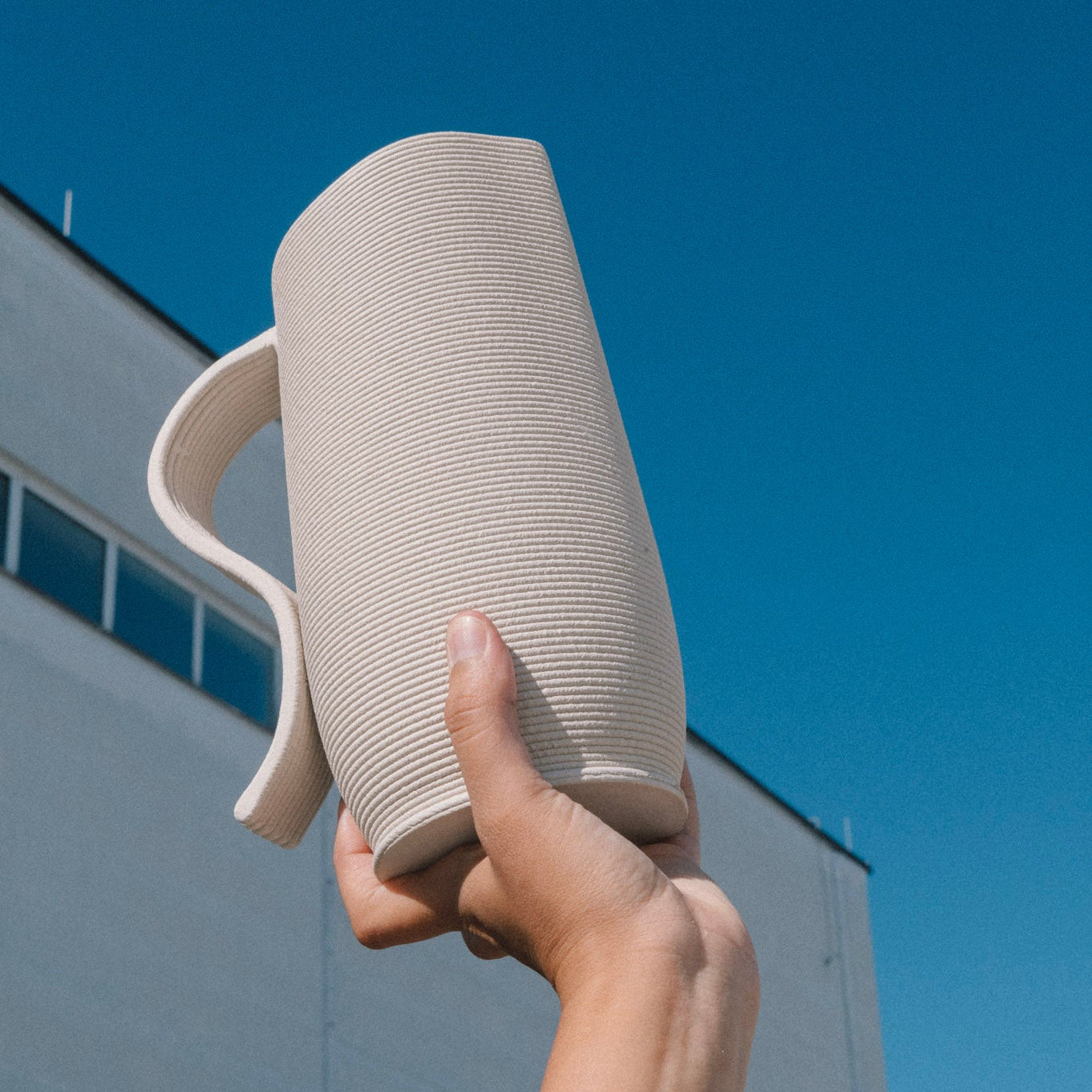 3D printed ceramic pitcher with sculptural handle, 3D Printed Ceramics and handmade in Berlin, minimal stoneware design photographed outdoors against blue sky.