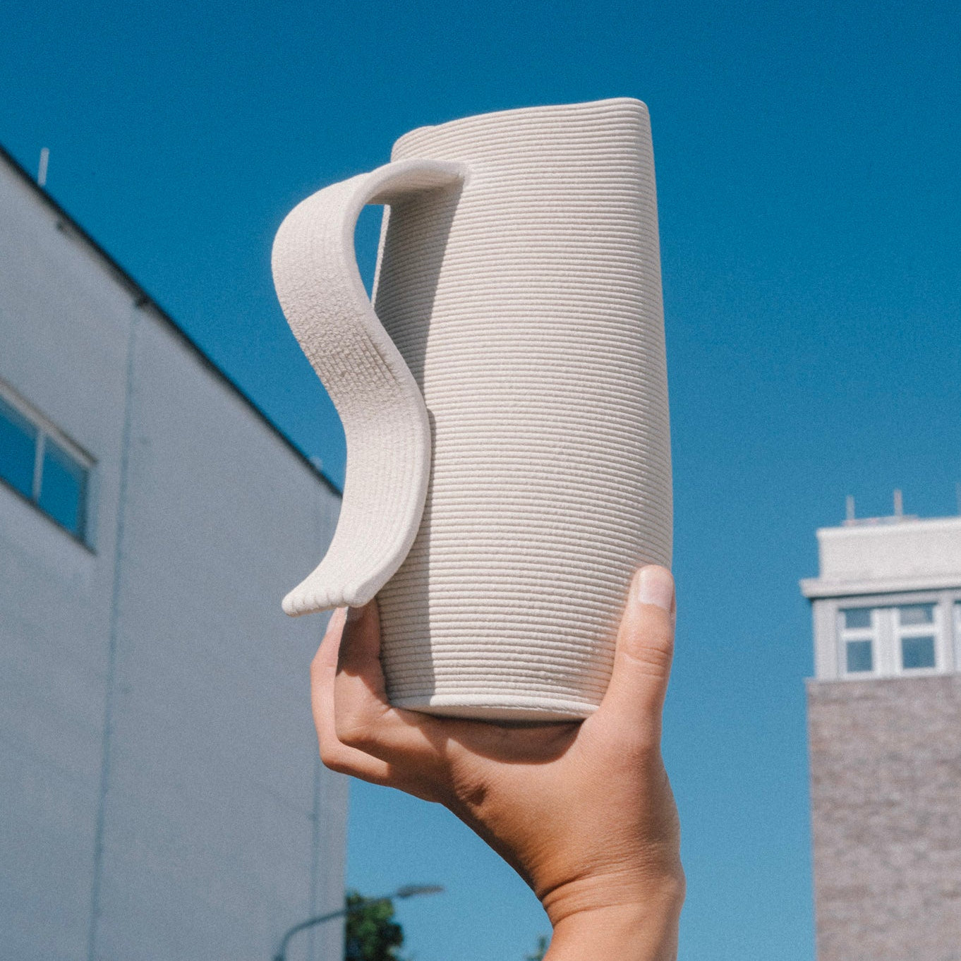 3D printed ceramic pitcher with sculptural handle, 3D Printed Ceramics and handmade in Berlin, minimal stoneware design photographed outdoors against blue sky.