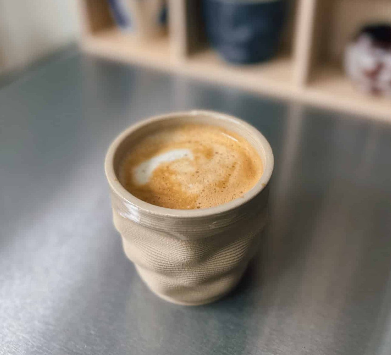 Cup of coffee on a metallic surface with a blurred bookshelf in the background