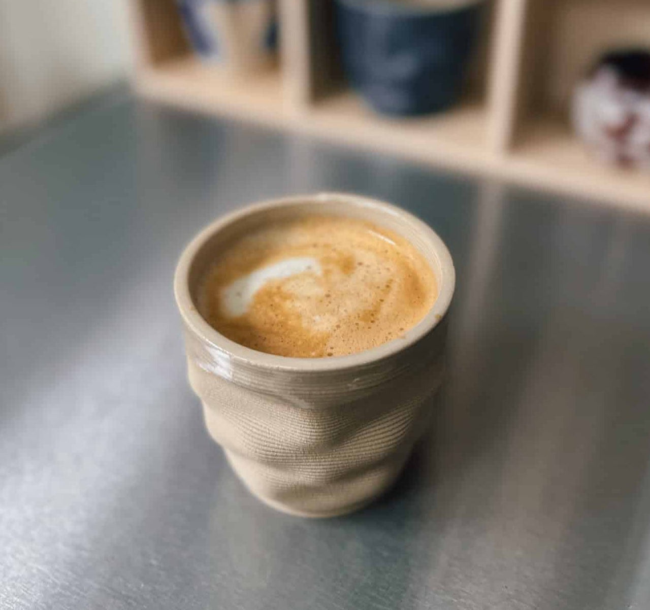 Cup of coffee on a metallic surface with a blurred bookshelf in the background