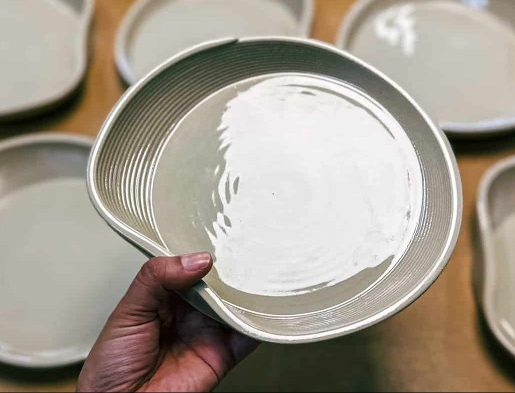 Hand holding a ceramic plate among other plates on a wooden surface. 3D Printed Ceramics Berlin