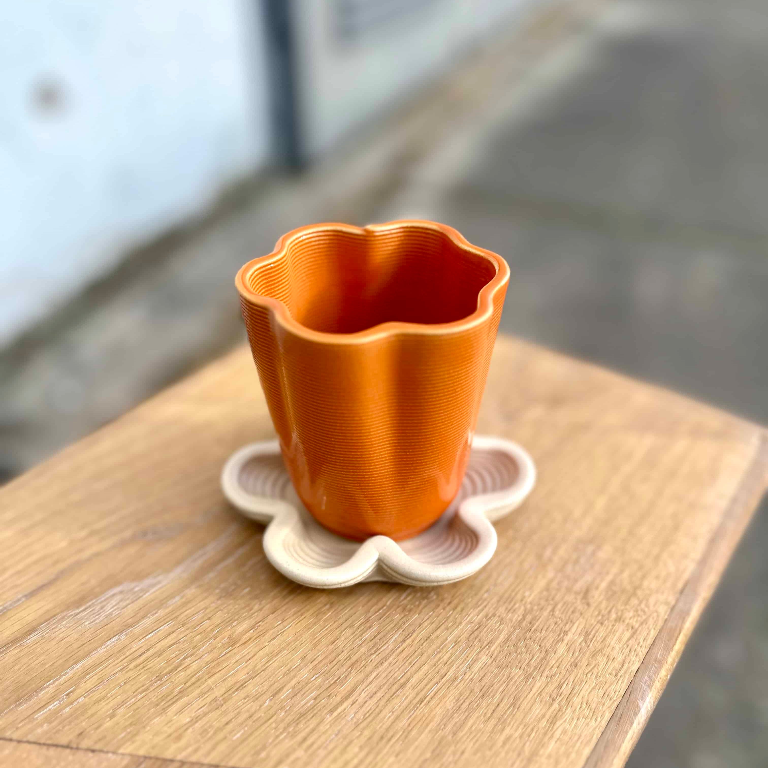 Flora Tray and Flora Cup — 3D printed ceramic flower-shaped cup and underplate handmade in Berlin, stoneware clay with orange glaze, modern design.
