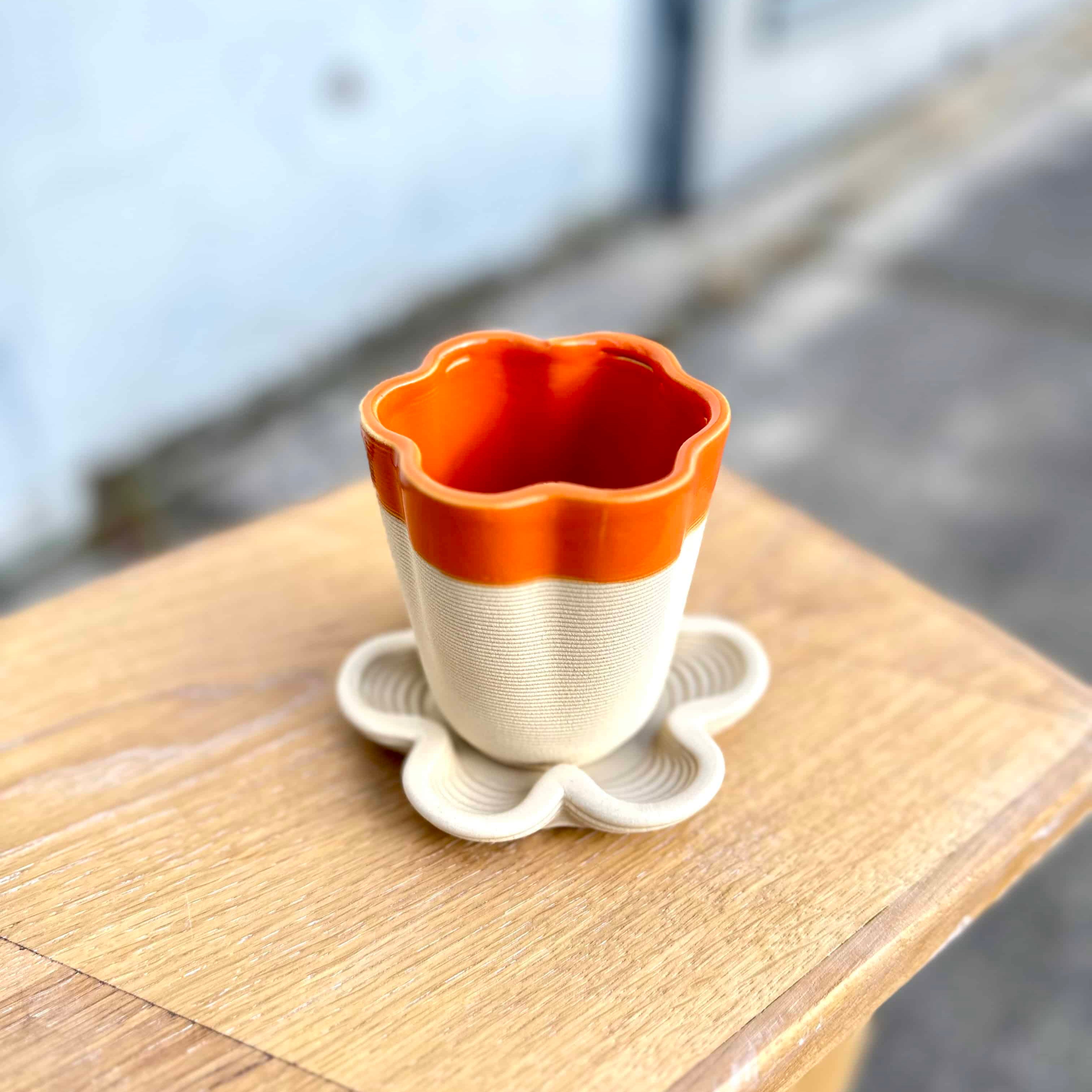 Flora Tray and Flora Cup — 3D printed ceramic flower-shaped cup and underplate handmade in Berlin, stoneware clay with orange glaze, modern design.